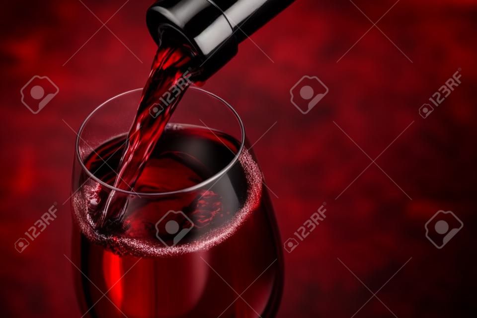 Strömender Rotwein in das Glas gegen Holzuntergrund