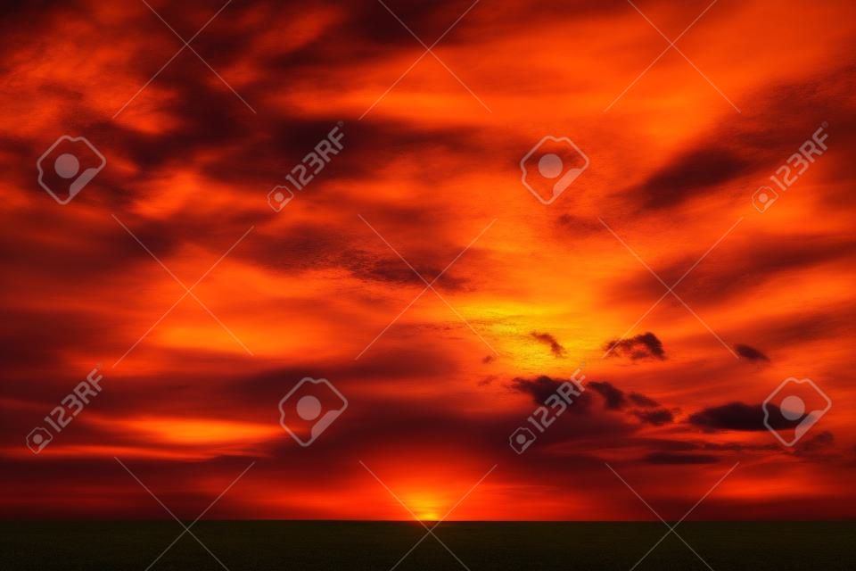 Hermoso paisaje ardiente de la puesta del sol en el prado y el cielo anaranjado sobre él.