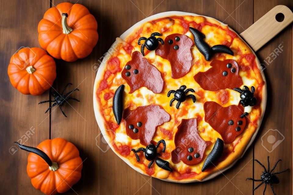 Halloween pizza with ghosts and spiders, above scene with decor on a rustic wood background