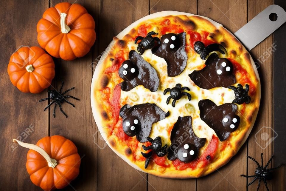 Halloween pizza with ghosts and spiders, above scene with decor on a rustic wood background