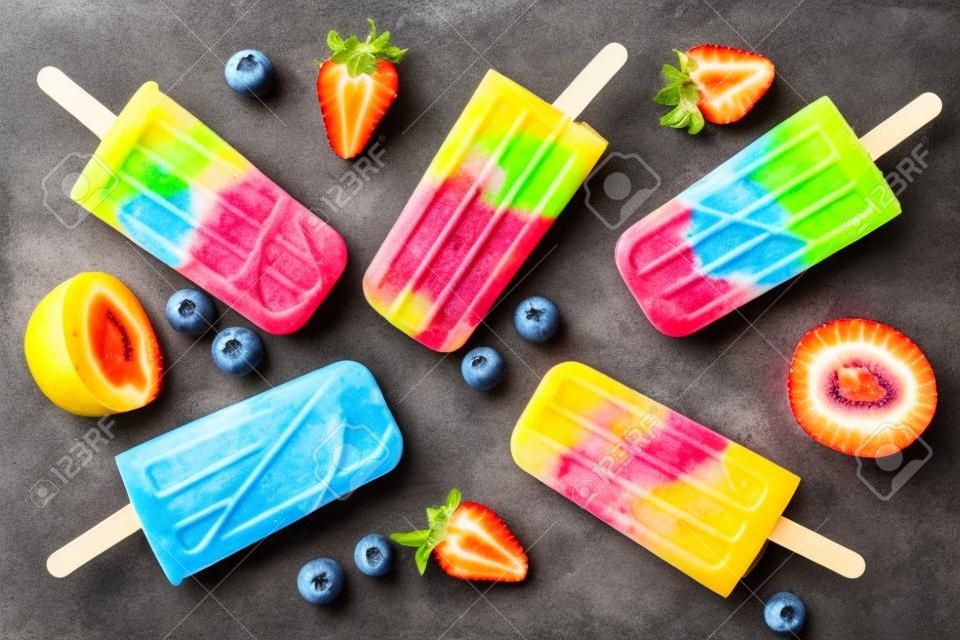 Healthy mixed fruit summer popsicles, top view scattered on a rustic dark