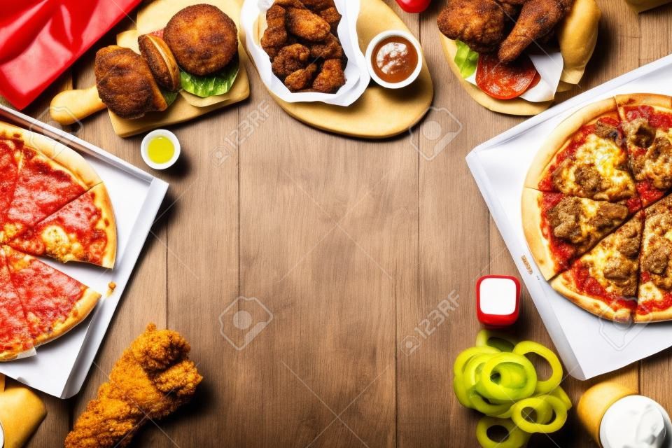 Frame with a variety of take out and fast foods. Pizza, hamburgers, fried chicken and sides. Top view on a white wood background with copy space.
