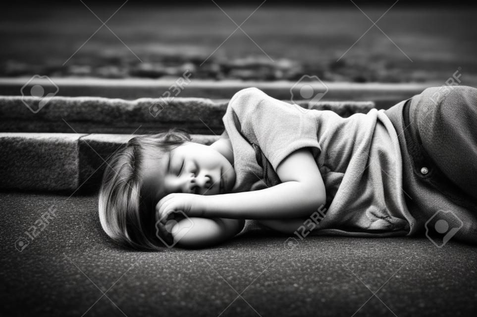 眠っているアスファルトの上の若い女の子の肖像画。黒と白の写真