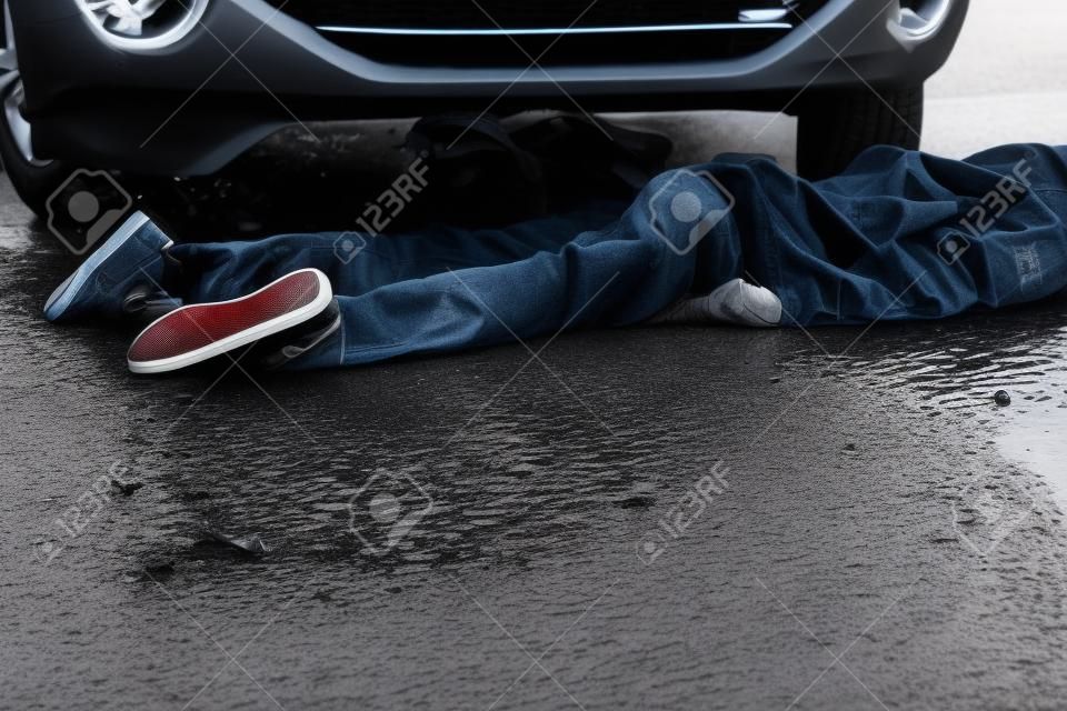 Close Up of Unrecognizable Car Accident Fatality - Bottom Half and Legs of Young Teenage Boy Car Accident Victim Lying on Wet Road Pavement in front of Stopped Vehicle