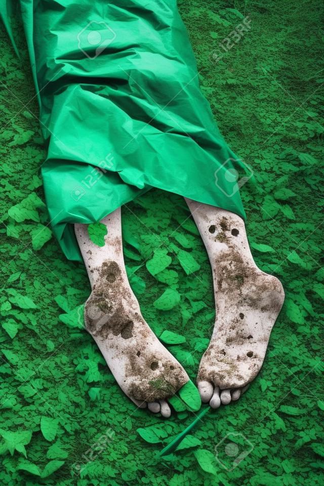 Verlassene Körper des Mordopfers mit barfuss aus Plane Blatt vorstehenden Körper auf grünen Boden bedeckt