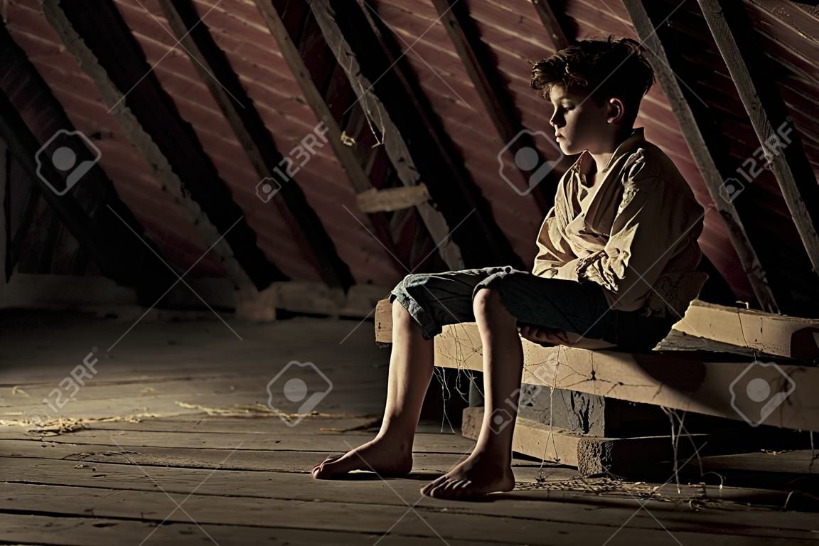 Boso nastoletni chłopiec unieruchomiony w prostej marynarce siedzi na drewnianej belce pokryte pajęczyny w zacienionym strychu w koncepcyjnym atmosferyczny obraz z miejsca kopiowania