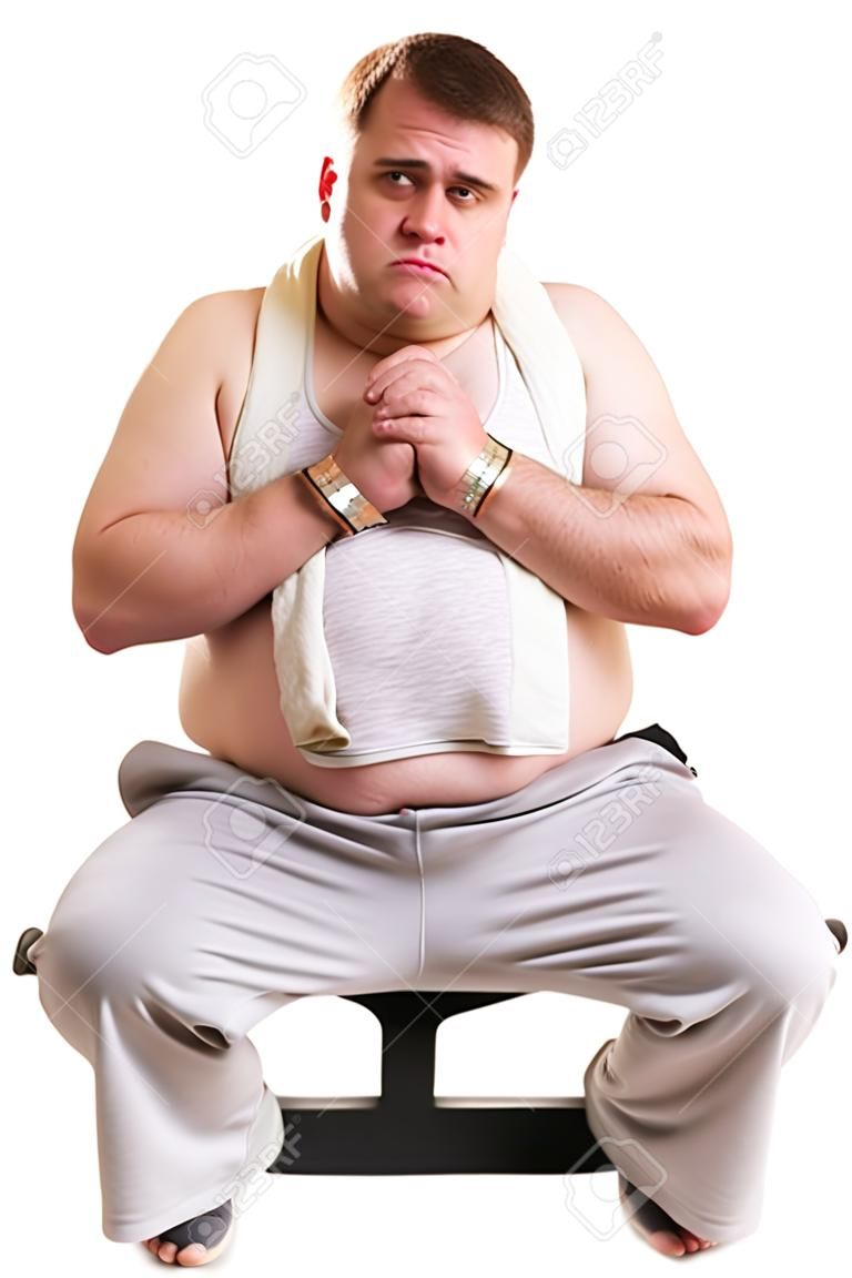 Overweight man resting on a bench for abdominals, tired after training, over white background