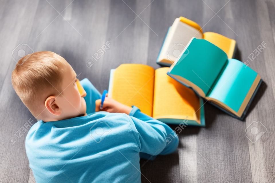 Mały chłopiec dziecko czyta książkę. Leży na podłodze.
