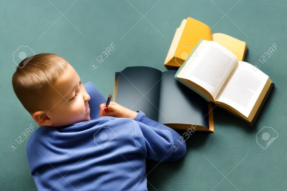 Mały chłopiec dziecko czyta książkę. Leży na podłodze.