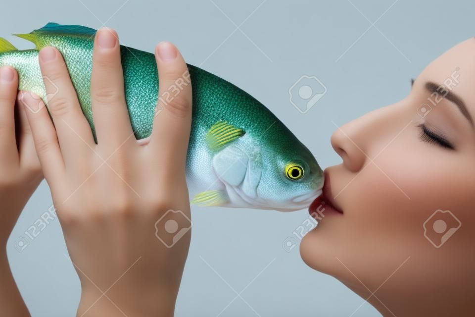 Beautiful young woman with closed eyes kissing a fish, isolated on white