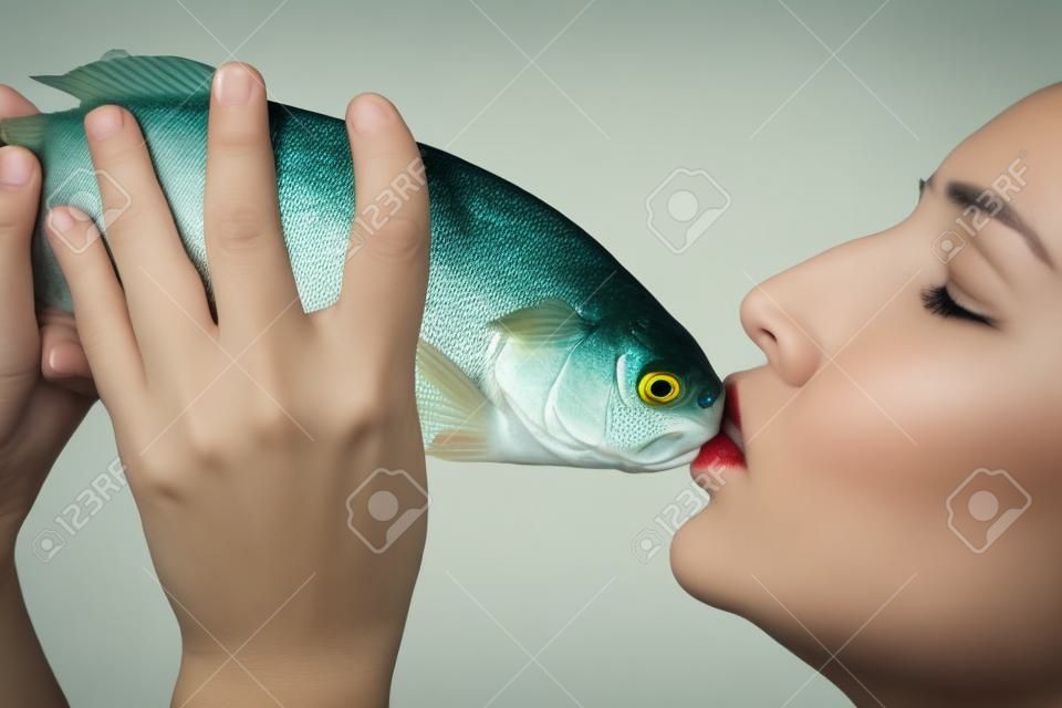 Beautiful young woman with closed eyes kissing a fish, isolated on white