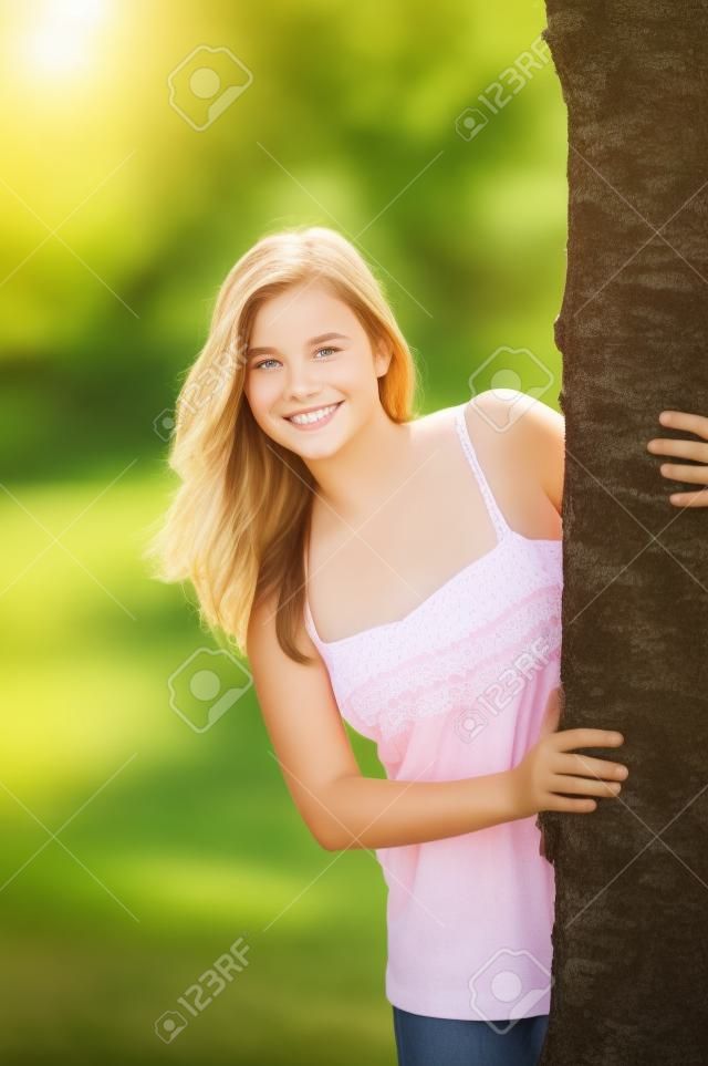 Odkryty portret cute nastolatka za drzewem w lecie