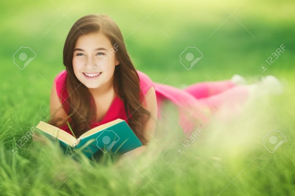 可愛的青少年戶外人像讀一本書，而躺在綠草