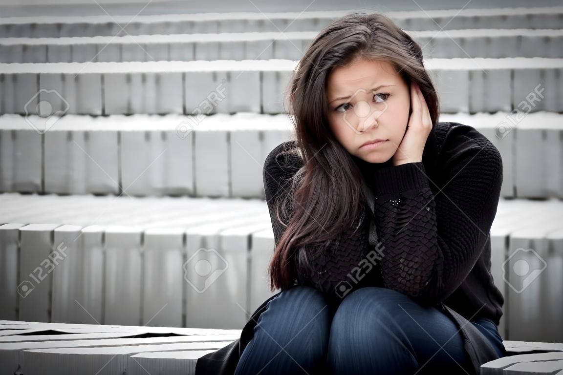 Outdoor portrait of a sad teenage girl looking thoughtful about troubles in front of a gray wall