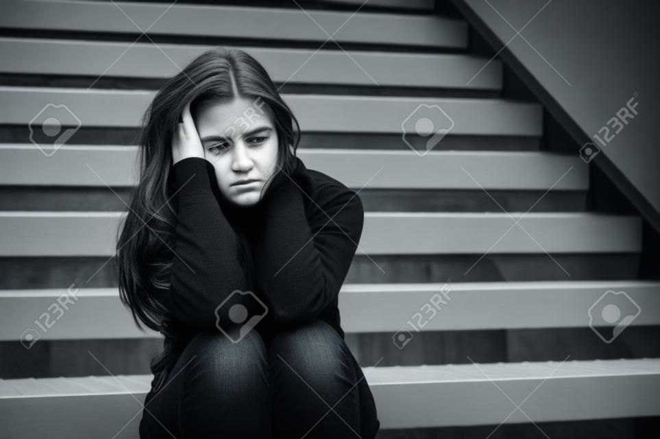 Retrato al aire libre de una joven mujer triste mirando pensativo sobre apuros, sentado en la escalera de metal, monocromo