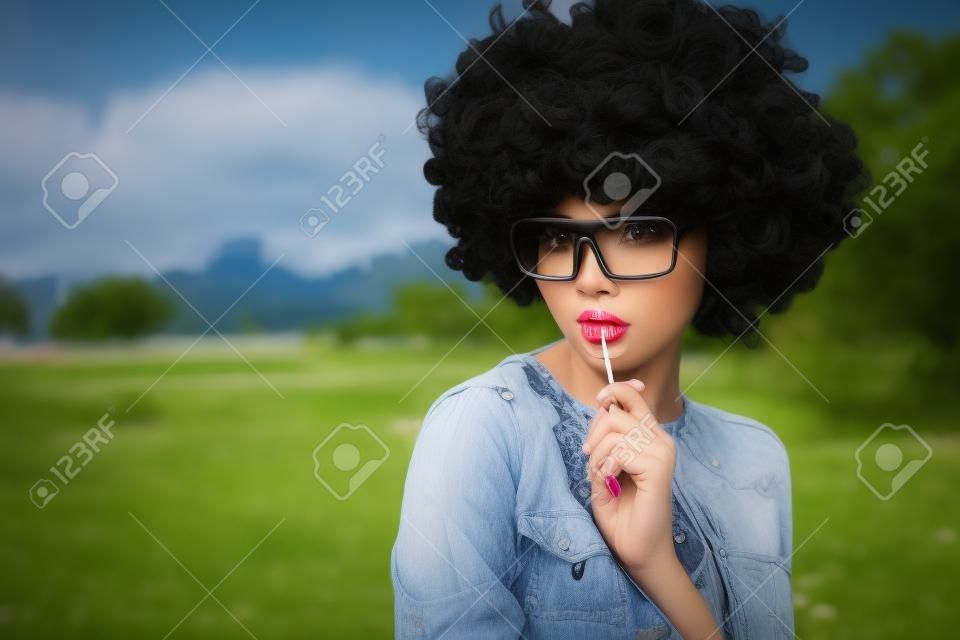 girl with black wig hair sucks lollipop. Outdoors lifestyle