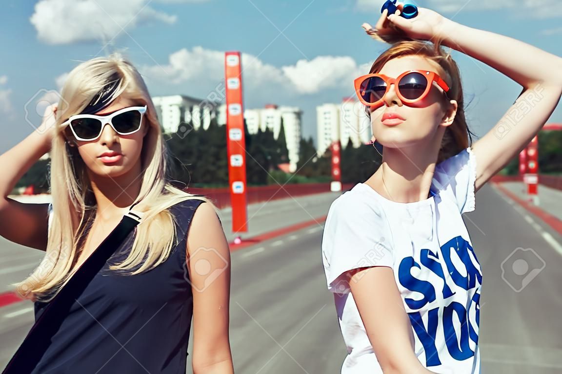 Две красивые счастливые девушки в темных очках, глядя в расстоянии на фоне городских. Молодые активные люди. На открытом воздухе