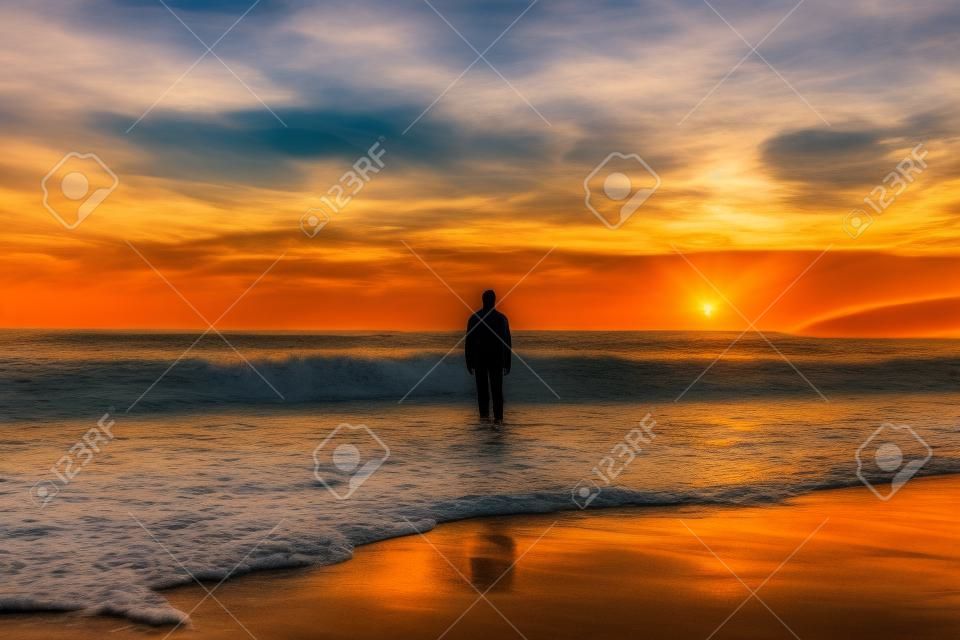 Homme debout sur la plage au coucher du soleil avec vue sur l'océan
