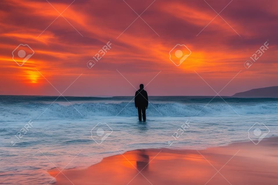 Homem de pé na praia ao pôr do sol com vista para o mar