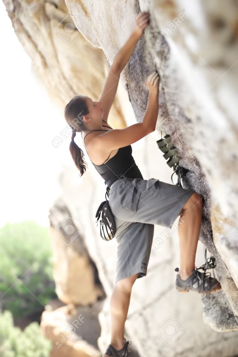 Jonge mooie vrouw die op een rotsmuur klimt.