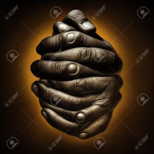 Low key, close up of hands of a faithful mature man praying, hands folded, interlaced fingers in worship to god. Isolated black background. Concept for religion, faith, prayer and spirituality.