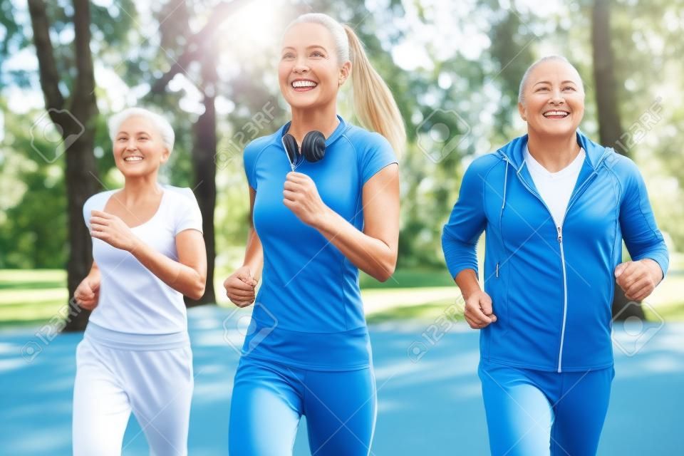 老人和妇女和年轻女性教练员锻炼在新鲜空气。户外活动，健康的生活方式，强壮的身体，健康的身材。时尚，现代的运动服。不同的世代