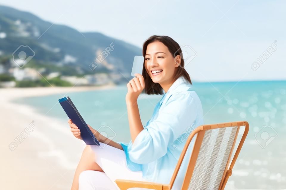 Donna felice con tablet digitale e carta di credito che acquista online seduto vicino al mare.