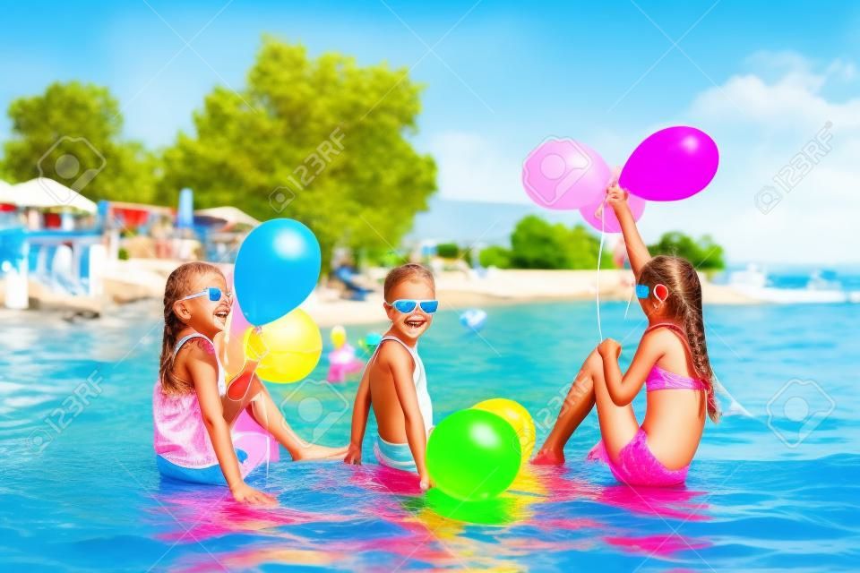Happy children playing with balloons in the sea. Kids having fun outdoors. Summer vacation and healthy lifestyle concept