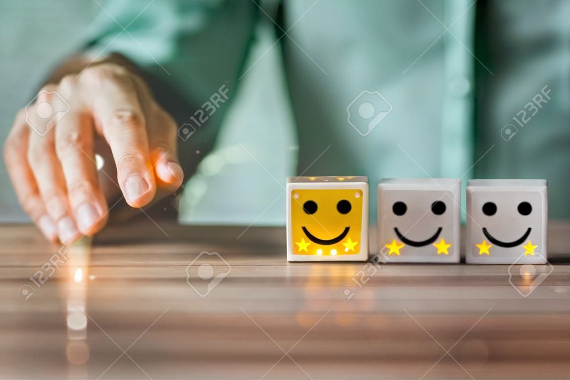 사업가의 손은 나무 큐브 블록에서 별 5개 만족도를 가진 웃는 얼굴 아이콘을 앞으로 움직입니다. 고객 서비스의 개념 최고의 우수한 비즈니스 평가 경험.