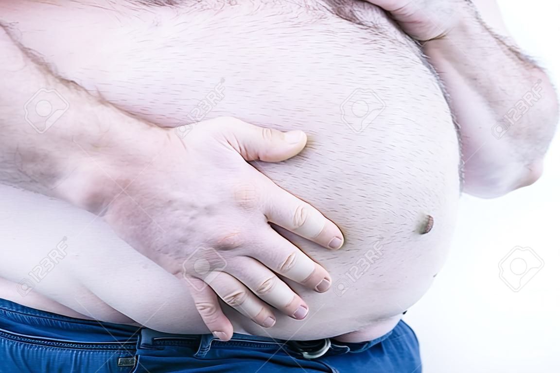 Ręka grubego mężczyzny trzymającego duży brzuch na jasnym tle: typowe zdjęcie brzucha piwnego: selektywna ostrość.