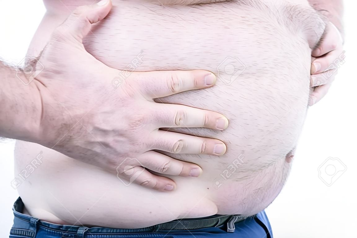 Ręka grubego mężczyzny trzymającego duży brzuch na jasnym tle: typowe zdjęcie brzucha piwnego: selektywna ostrość.