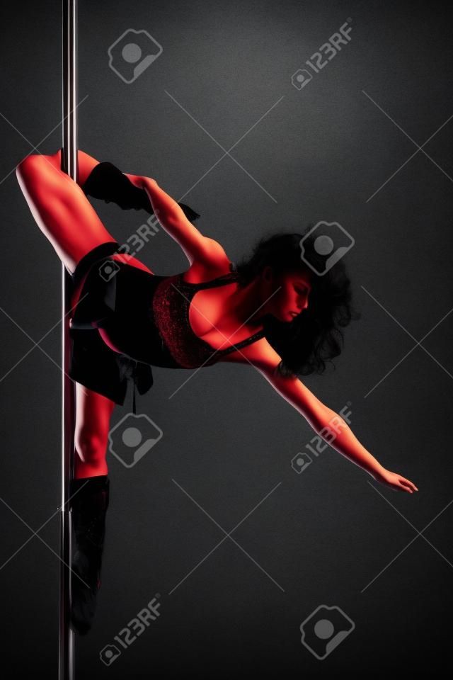 Junge schlanke Pole Dance Frau Ausübung auf einem dunklen Hintergrund
