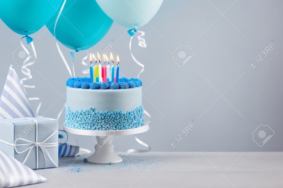 Blue Birthday cake, presents, hats and colorful balloons over light grey.