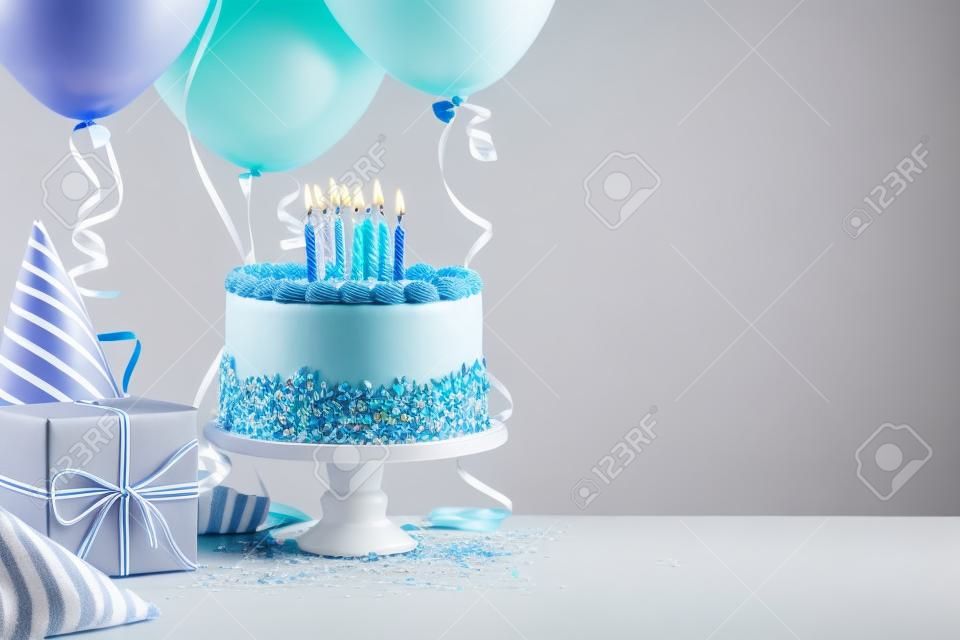 Blue Birthday cake, presents, hats and colorful balloons over light grey.