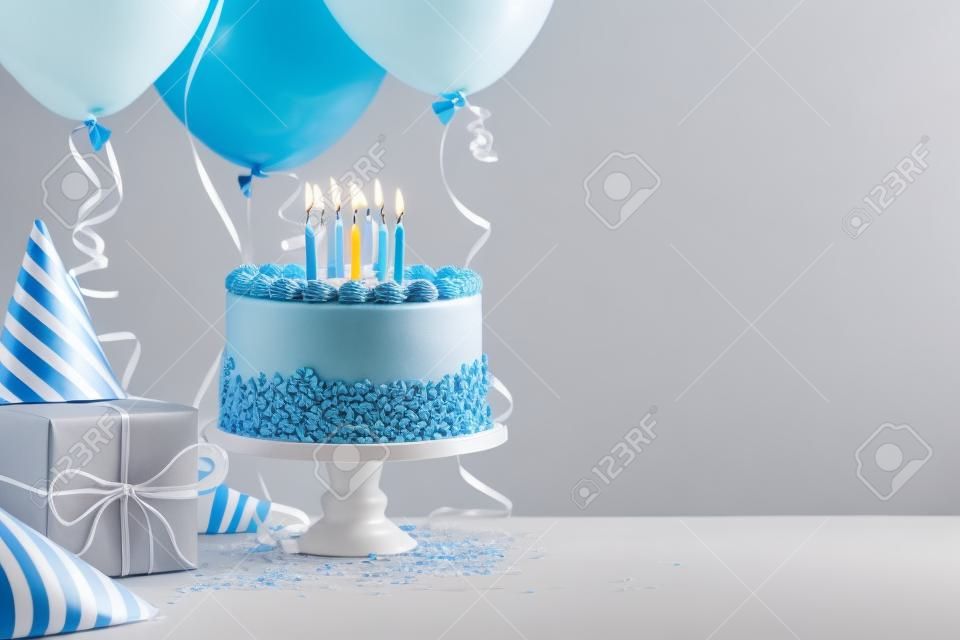 Açık renkli gri üzerinde mavi doğum günü pastası, hediyeler, şapkalar ve renkli balonlar.
