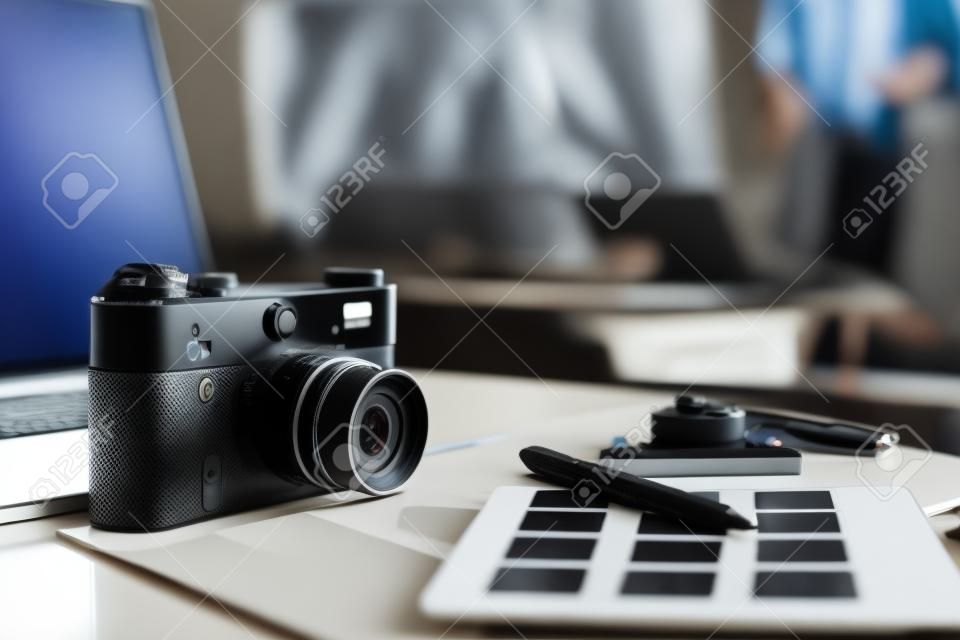 Laptop and camera on the desk , two businesspeople standing in the background.