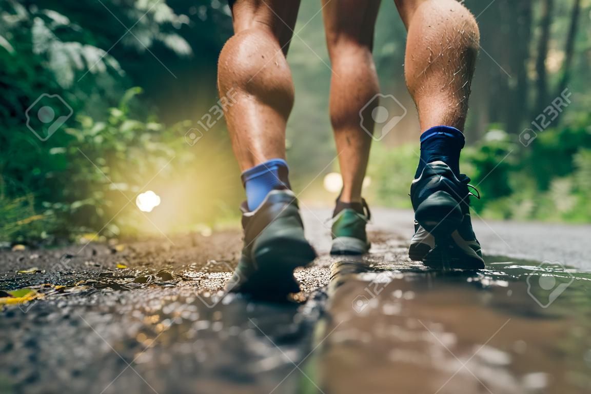 Boves musculosos de treinamento de corredores masculinos aptos para corrida de trilha de floresta de cross country na chuva em uma trilha de natureza.