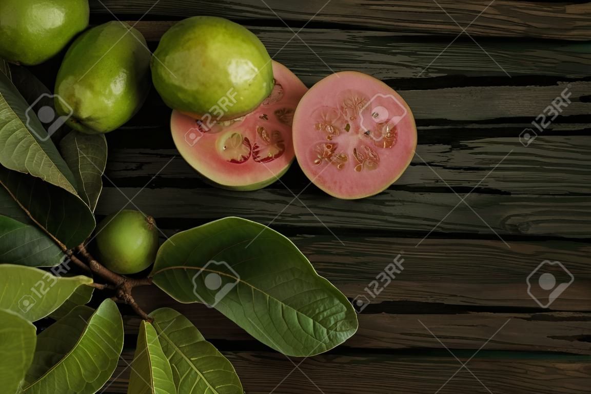 Fresh red guavas with green leaves on wooden demolition background. Wood texture and guava leaves.