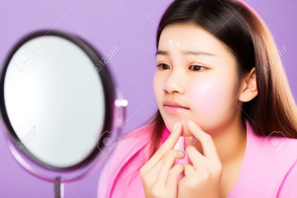 Asian teenage woman  looking at mirror and squeeze acne problem on her face, skin care concept.