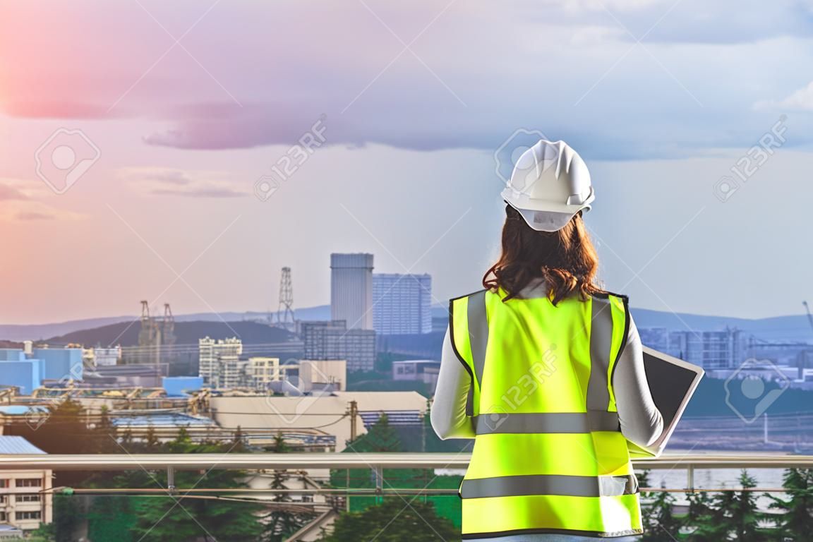 Female Civil engineer with computer and blueprint is standing infront Japan industry city in background.