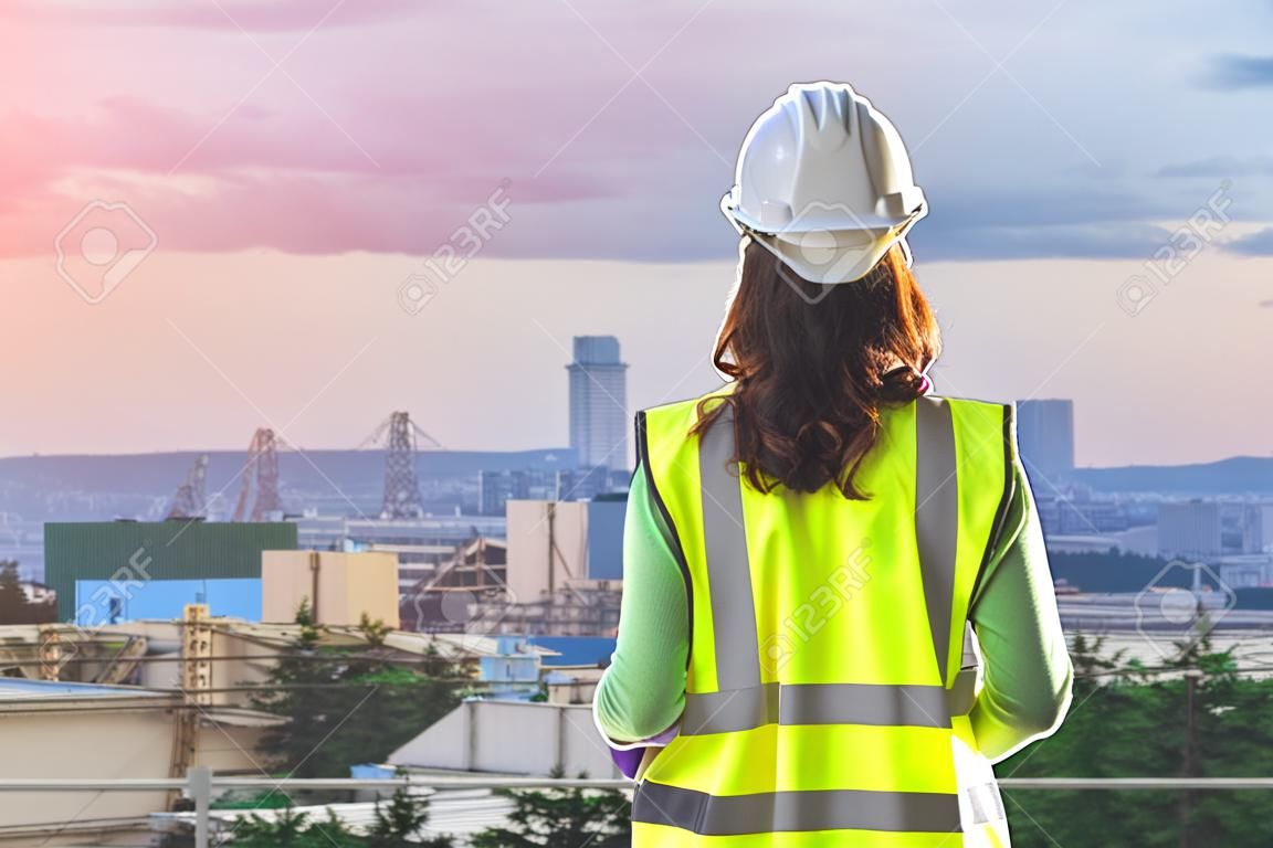 Female Civil engineer with computer and blueprint is standing infront Japan industry city in background.