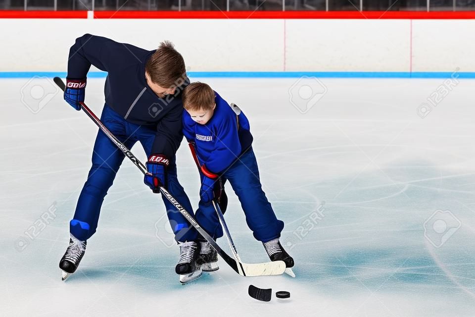 Father with his little son playing ice hockey