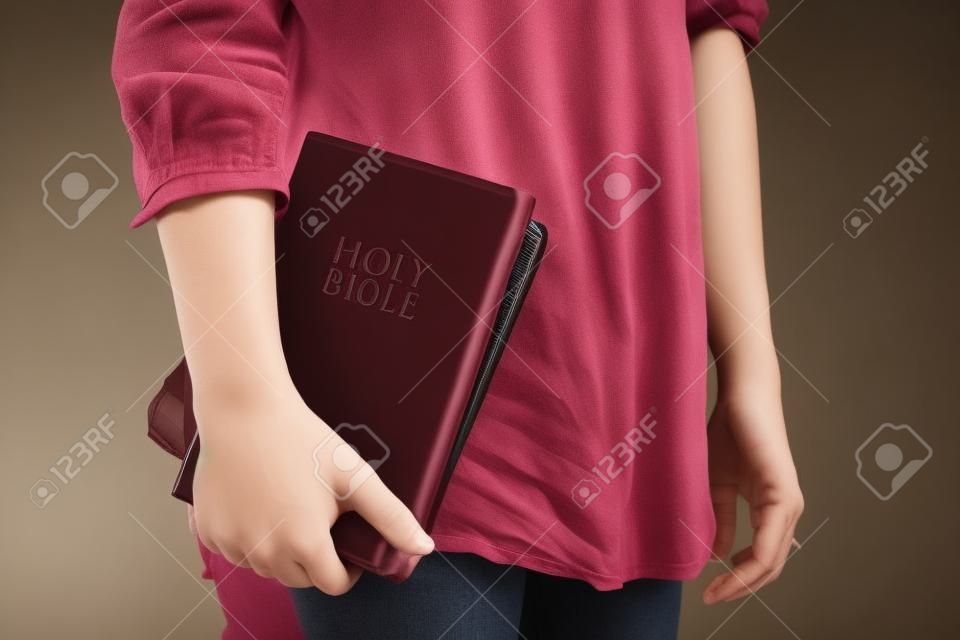 Egy fiatal nő áll bent véletlenül gazdaság egy gesztenyebarna Bibliát mellé.