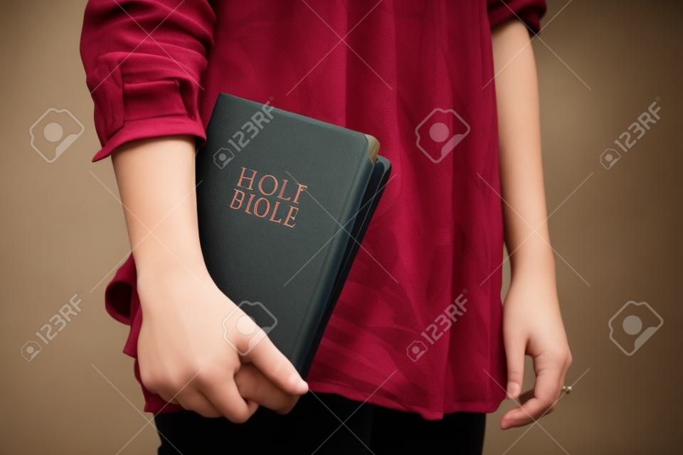Egy fiatal nő áll bent véletlenül gazdaság egy gesztenyebarna Bibliát mellé.