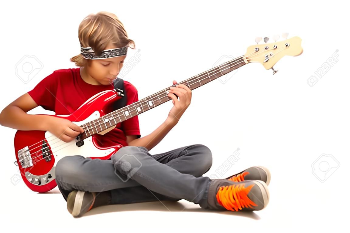 Teen boy sitting on floor with legs crossed and playing bass guitar isolated on white background