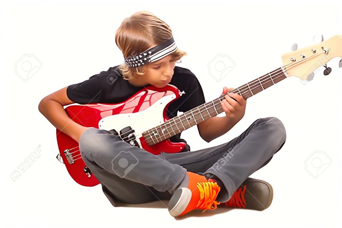 Menino adolescente sentado no chão com as pernas cruzadas e tocando baixo isolado no fundo branco