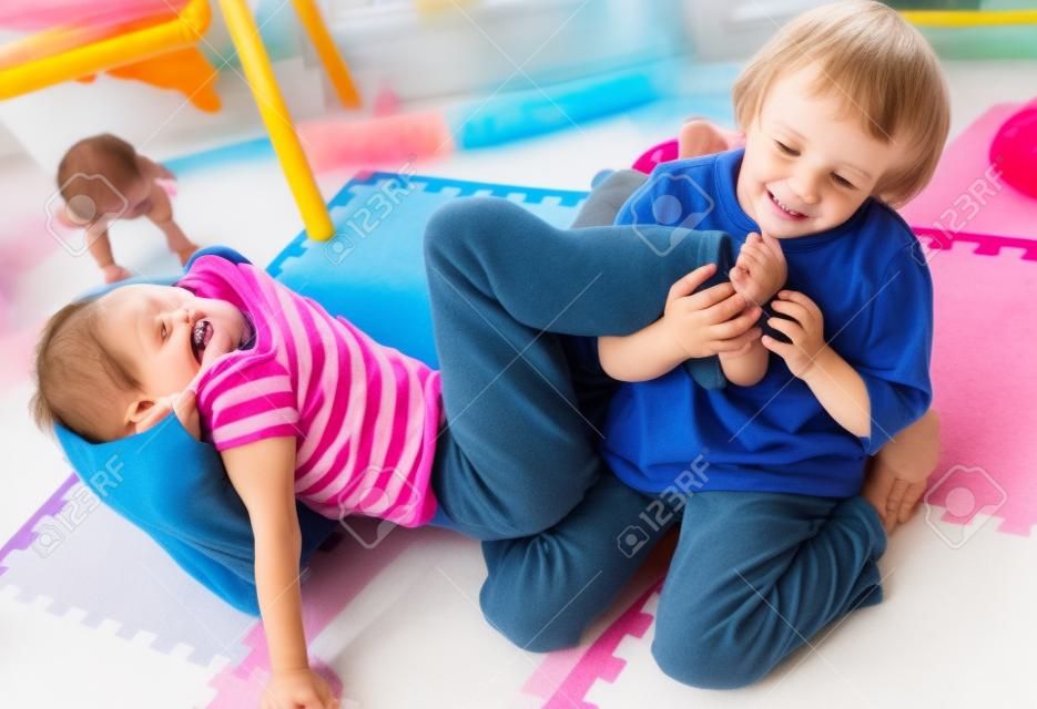 Adorable twins lucha/jugando mantener ubicación en el piso de la sala de juegos.