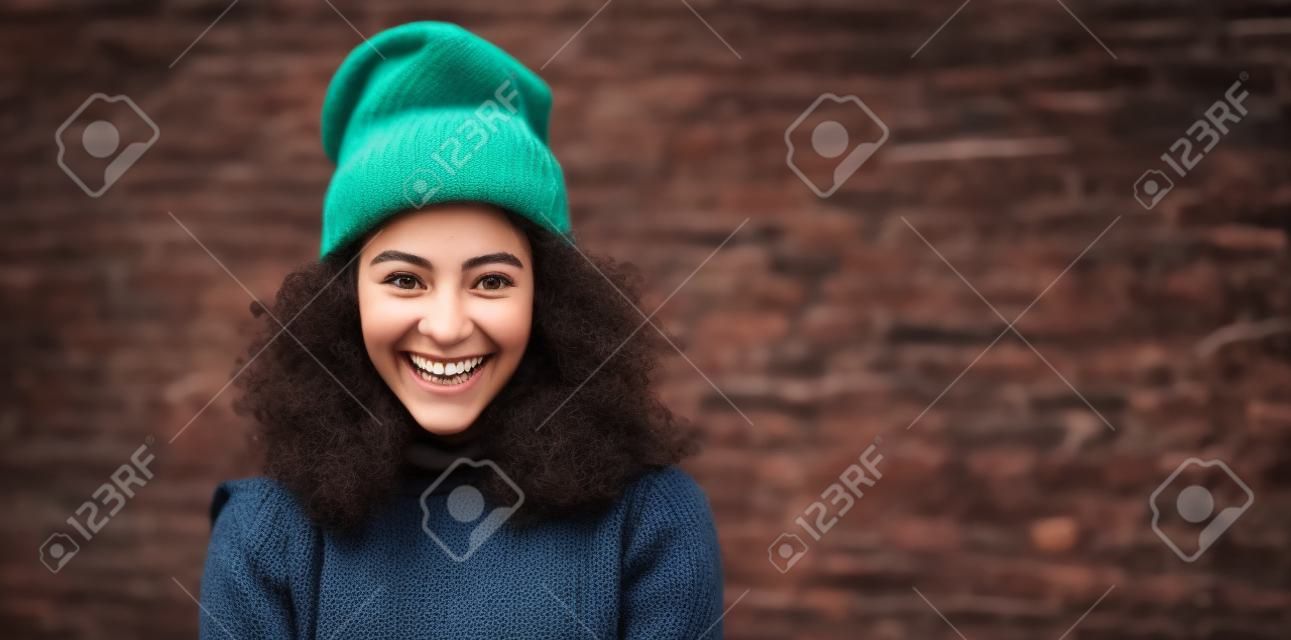 Śmiejąca się młoda dorosła kobieta z Ameryki Łacińskiej w czapce z dzianiny w miejskim stylu
