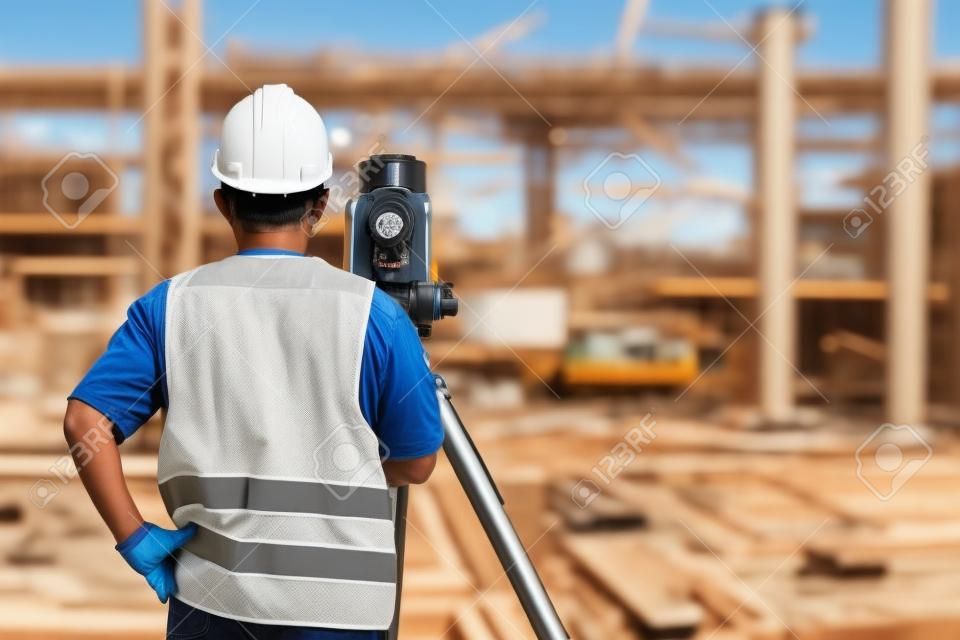 Retrato del trabajador de construcción con el equipo teodolito de tránsito en el lugar de construcción al aire libre durante el trabajo de topógrafo