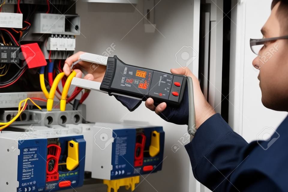 Eletricista trabalha. técnico masculino examinando fusebox com pinça digital multímetro ac dc testador